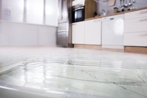 Flooded kitchen floor with water spreading across the white tiles