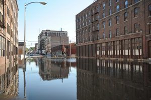 Flooded street between brick buildings, with reflections in standing water.