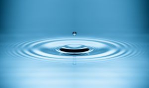 A water droplet creating ripples on a calm blue surface