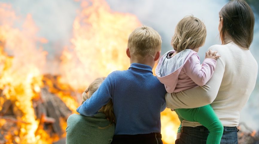 People carrying children away from a large fire and smoke outdoors