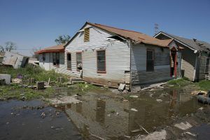 Flood-damaged house with muddy standing water and debris in the yard