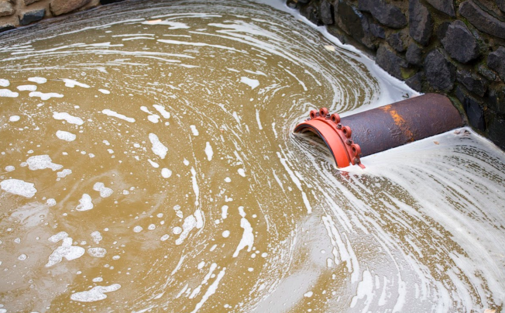 Pipe discharging foamy water into a muddy pond, creating swirling currents