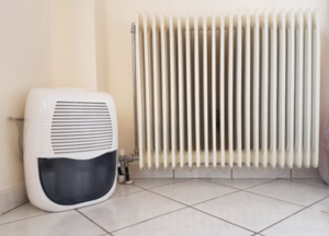 Dehumidifier beside a white radiator on a tiled floor in a room corner