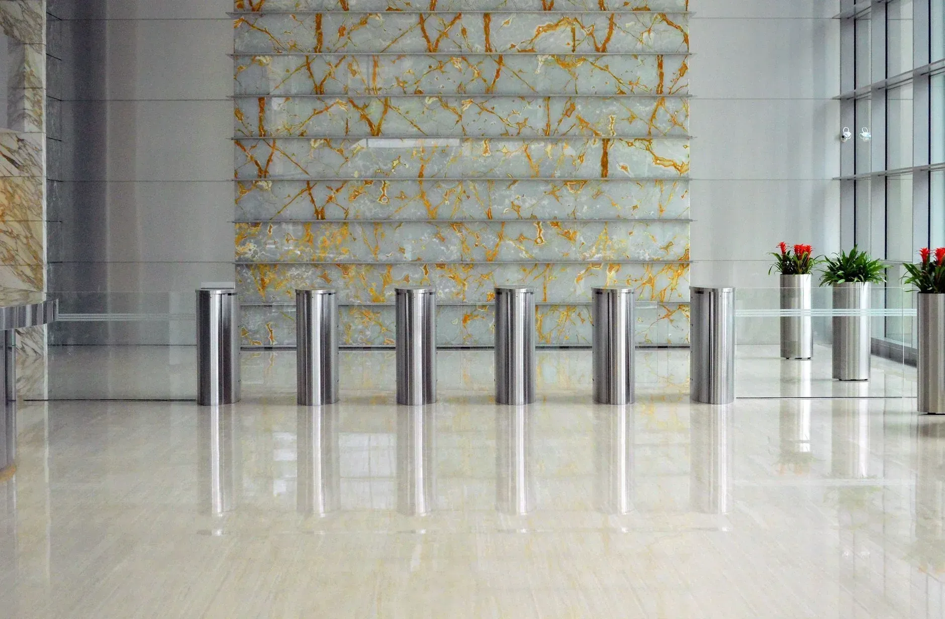 Modern lobby with metal turnstiles, polished floor, stone wall, and potted plants by large windows