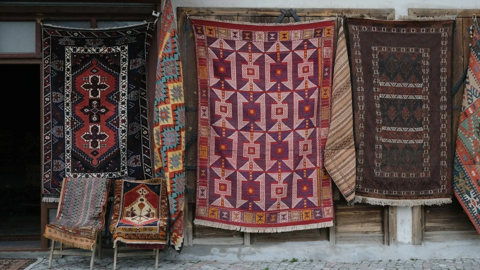 Assorted colorful woven rugs hanging in a market stall, with geometric patterns and earthy tones