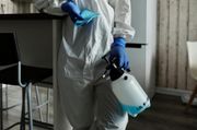 Person in white protective suit and blue gloves carrying a spray disinfectant in a room