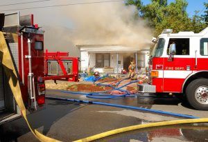 Firefighters battling a house fire with hoses and trucks amid heavy smoke and debris