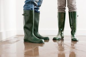 Two people wearing green rain boots standing on a wet reflective floor indoors