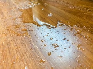 Water droplets on a wooden surface with a small puddle and bright reflection