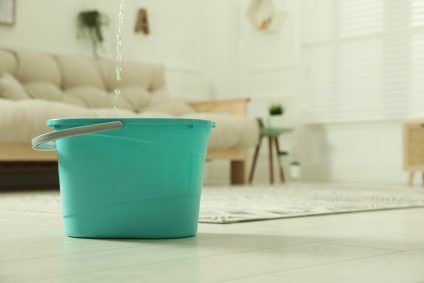 Turquoise bucket catching water on a bright living room floor
