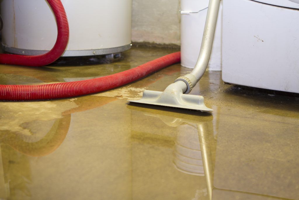 Flooded floor with a mop and red vacuum hose beside a white appliance