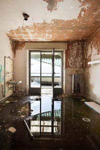 Flooded, dilapidated room with peeling walls and a reflective water-covered floor.