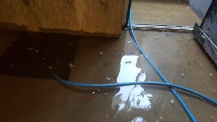 Blue hose crossing a wet floor beside a wooden cabinet and wall