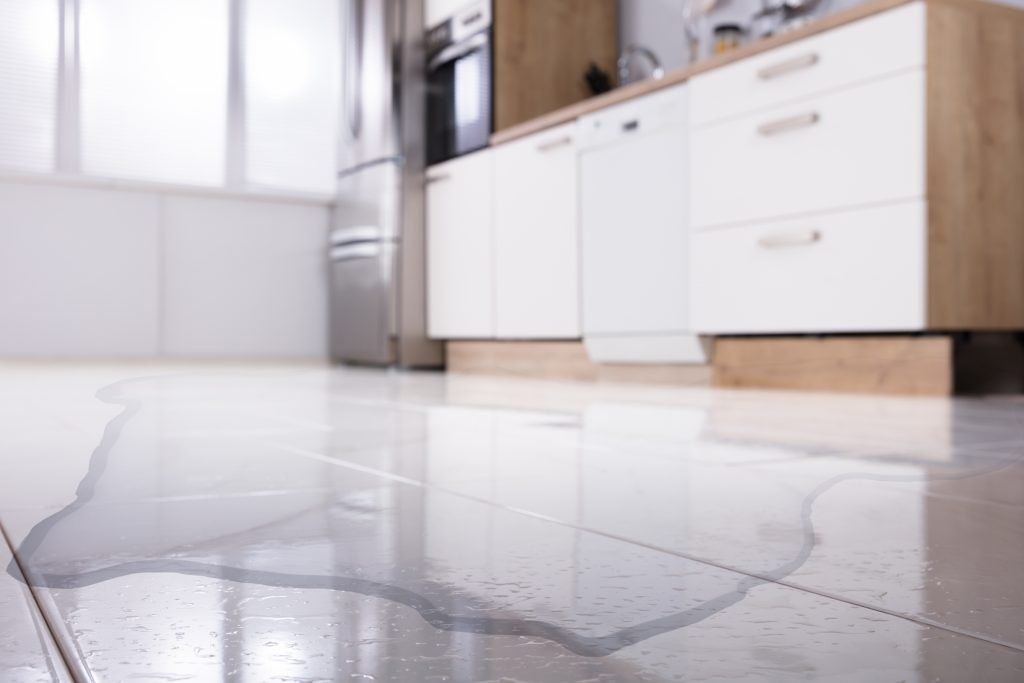 Kitchen floor with a large water leak puddle near white cabinets