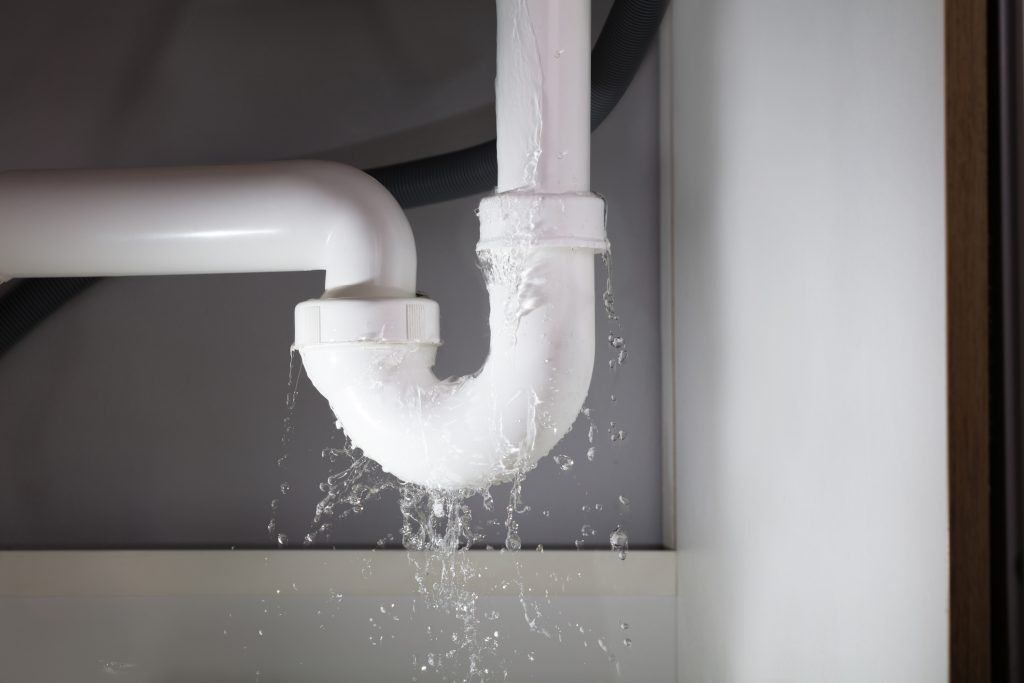 Leaking white drain pipe under a sink, with water dripping into the cabinet below
