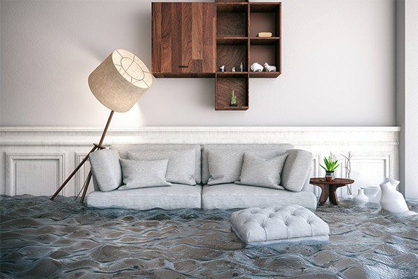 Flooded living room with gray sofa, tilted floor lamp, wall shelves, and submerged tufted ottoman