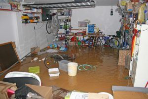Flooded basement with muddy water, scattered furniture, and cluttered belongings.
