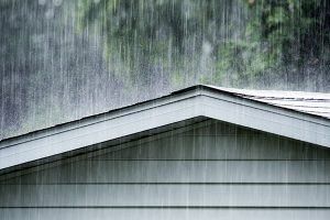 Rain pouring over a gray house roof and siding