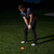 A person in dark golf attire addresses a glowing ball on a grassy course at night.