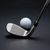 A white golf ball sits on a red tee next to a metal golf club head against a dark, minimalist background.
