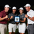 Four people in golf attire celebrate outdoors at night, holding a tablet displaying a QR code.
