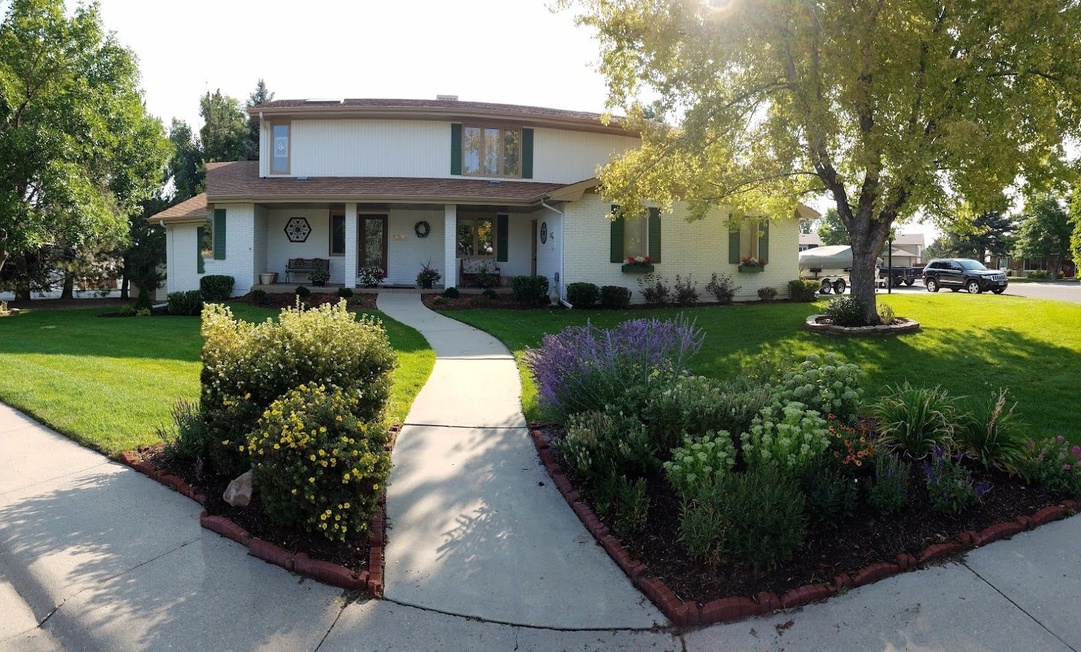 Suburban two-story house with a curved walkway, green lawn, and landscaped front garden in bright sunlight