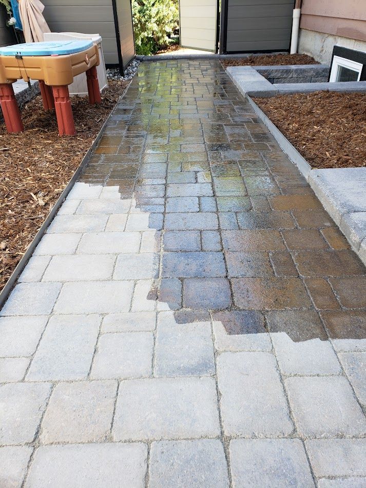Wet stone pathway between raised garden beds beside a house and patio area.