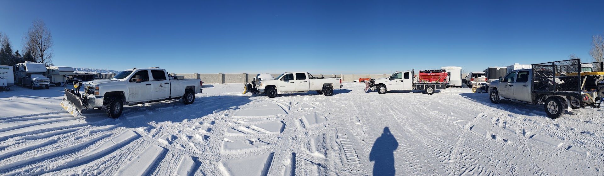 Parked pickup trucks and other vehicles on a snowy lot under a clear blue sky