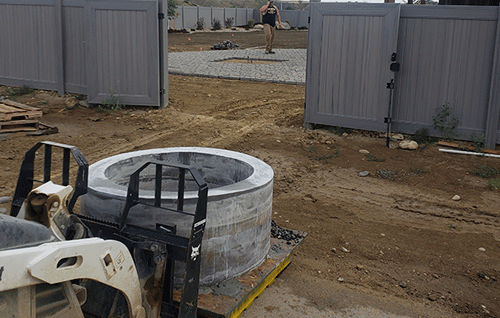 Construction site with a forklift lifting a concrete pipe near an open gate