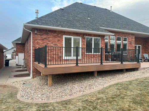 Brick house with raised wooden deck, black railing, and gravel landscaping.