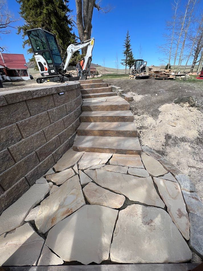 Cracked stone patio with steps beside a retaining wall, with construction equipment in the background