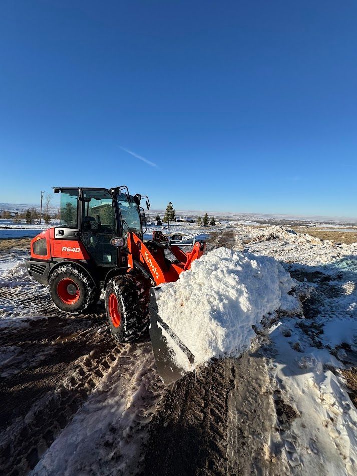 Orange tractor clearing snow on a rural road under a clear blue sky