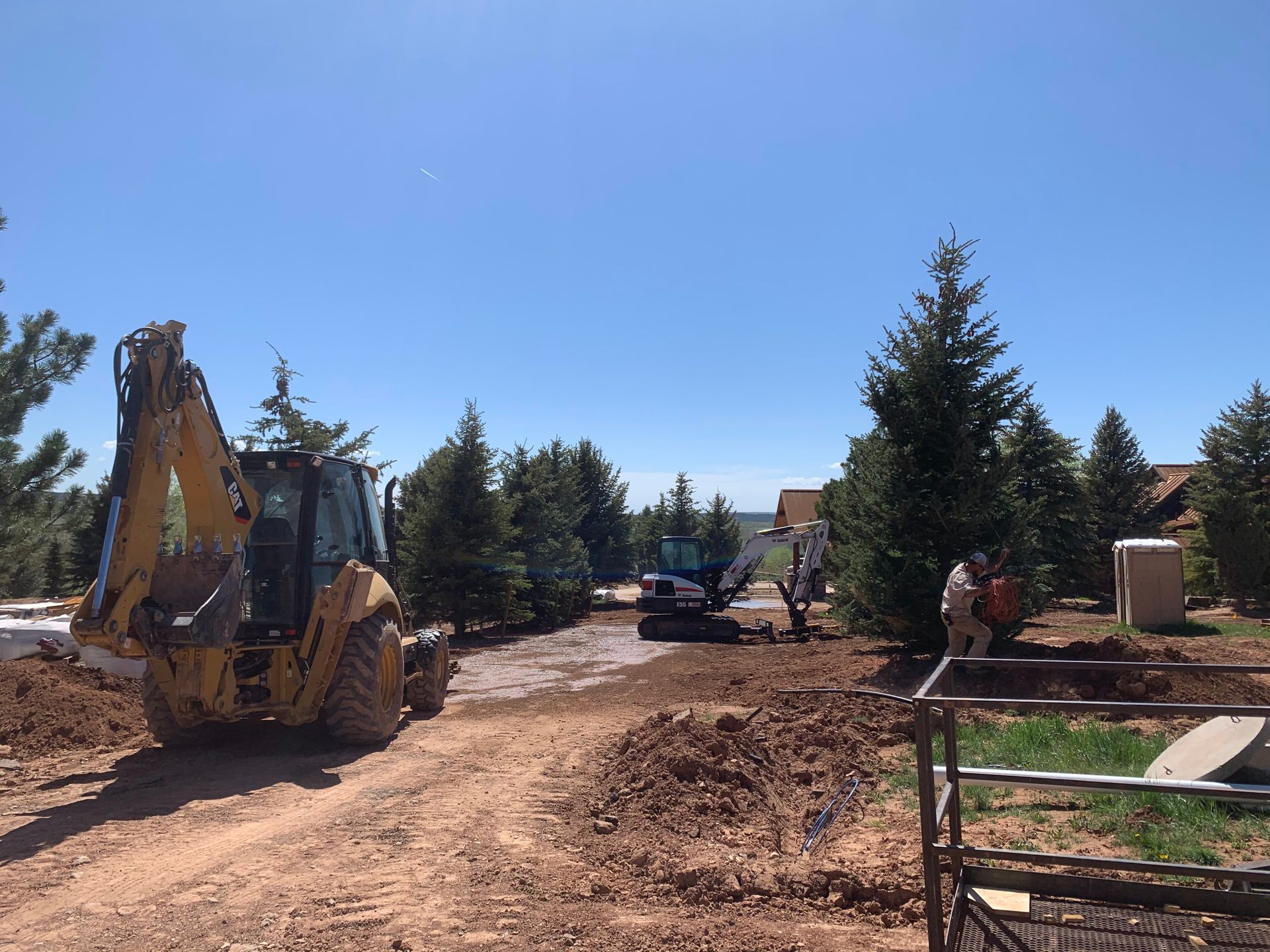 Yellow excavator on a dirt road at a rural construction site under a clear blue sky