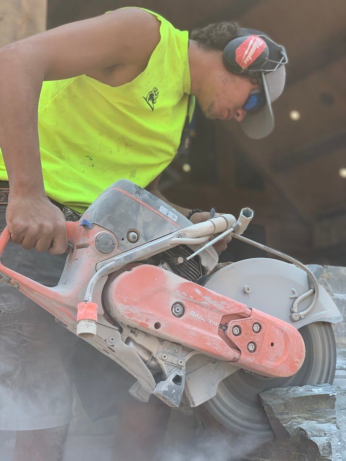 Worker in neon vest using a circular saw to cut stone, with dust in a construction setting