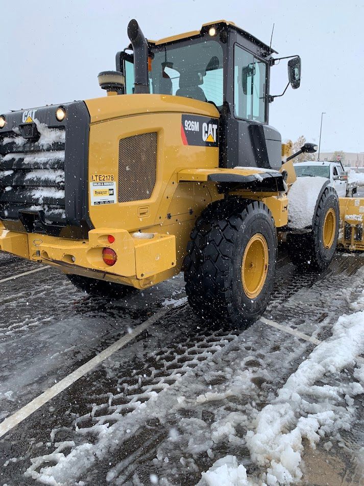Yellow snowplow clearing a snowy road, with a white truck behind it.