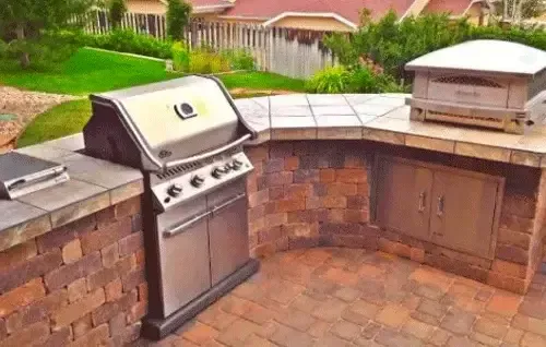 Built-in brick outdoor grill and stone counter in a backyard patio area
