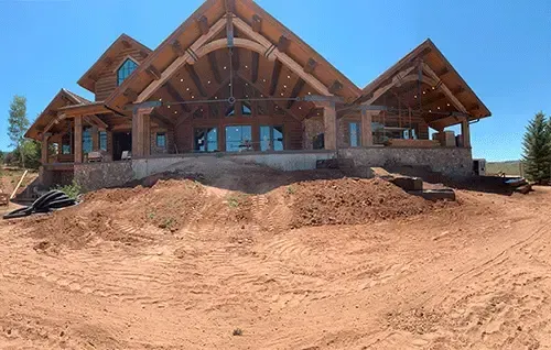 Partially built wooden house on a dirt lot under a clear blue sky
