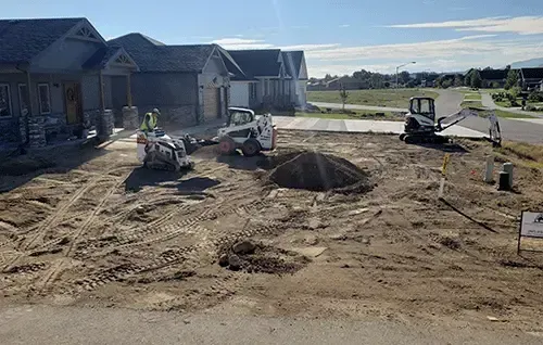 Construction site with excavators and dirt piles beside new houses on a sunny day