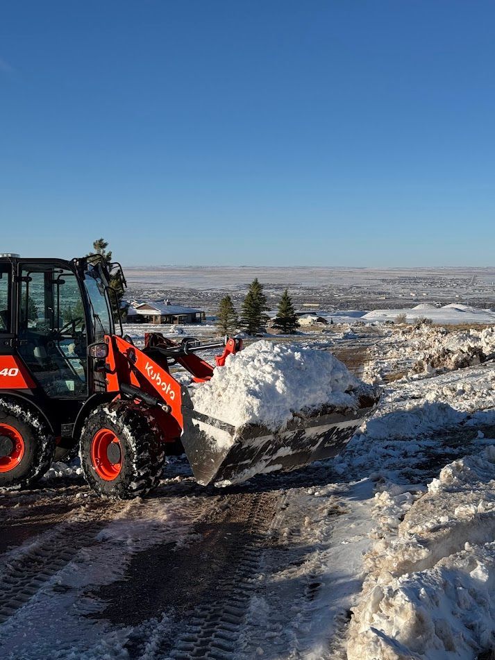 Orange snowplow clearing a snowy road with mountains in the background