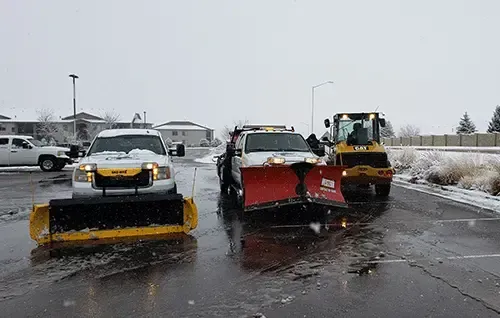 Three snowplows clearing a wet, slushy parking lot in winter.