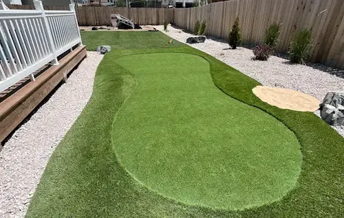 Backyard with artificial turf putting green bordered by gravel and a wooden deck fence