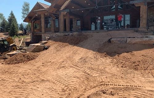House under construction with dirt driveway and stone facade on a sunny day