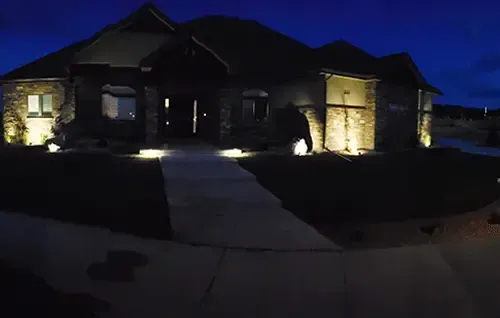 Dark suburban house at night with lit stone columns and a walkway leading to the front door