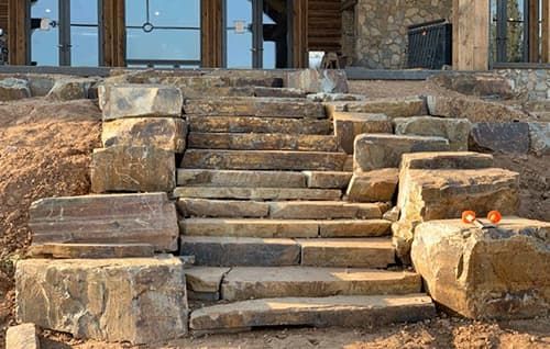 Stone steps leading to a building entrance, with rocks and wooden doors in a rustic outdoor setting