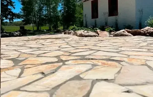 Stone-paved courtyard beside a white building with windows and trees in the background.