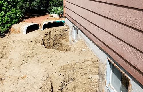 Construction site beside house with dirt piled against the foundation and drainage pipes visible