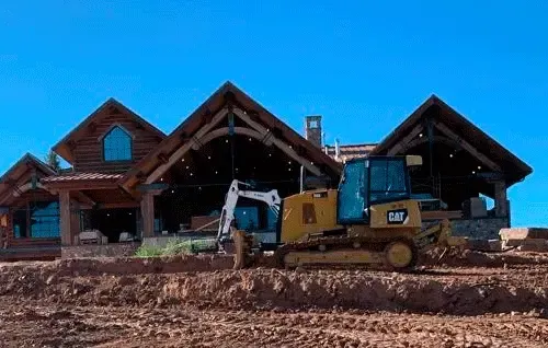 Bulldozer and backhoe at a large wooden house under construction on a dirt site