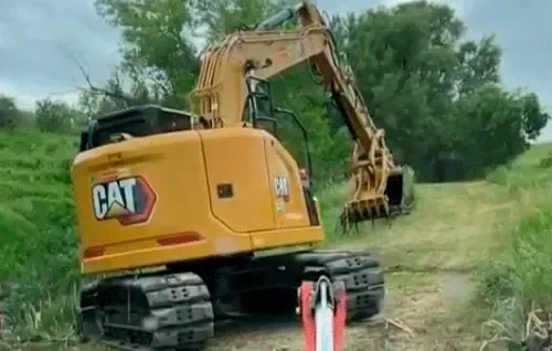 Yellow CAT excavator parked on a grassy field with its arm extended, trees in the background