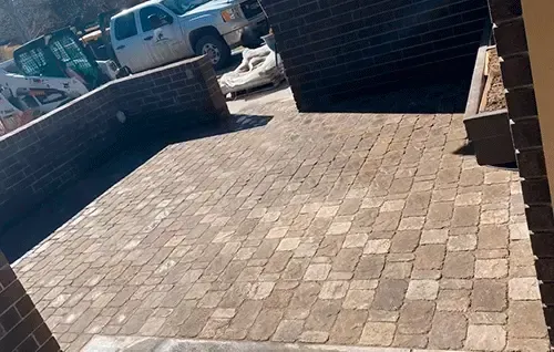 Brick-paved driveway or patio bordered by low brick walls, with parked vehicles in the background.