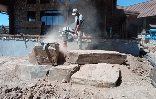 Worker cutting a large stone slab at a dusty construction site with a power saw
